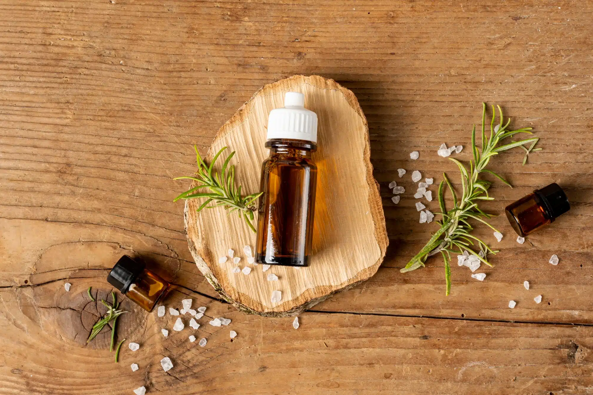 Amber bottles with green sprigs and pale crystals on a wooden surface