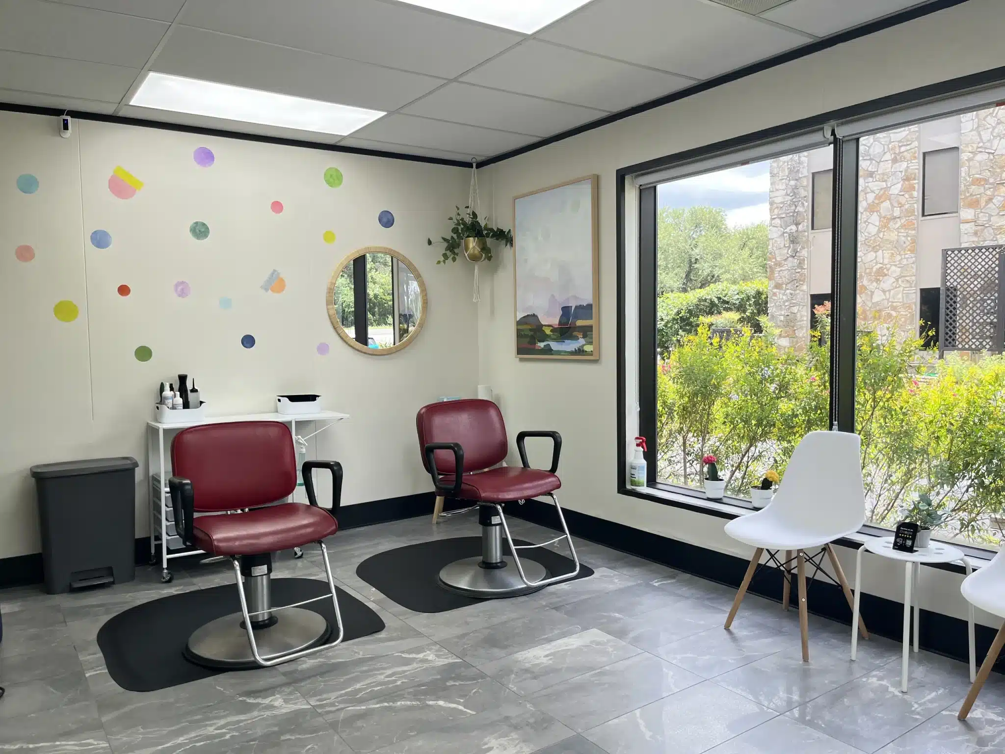Two burgundy salon chairs on black mats beside a large window