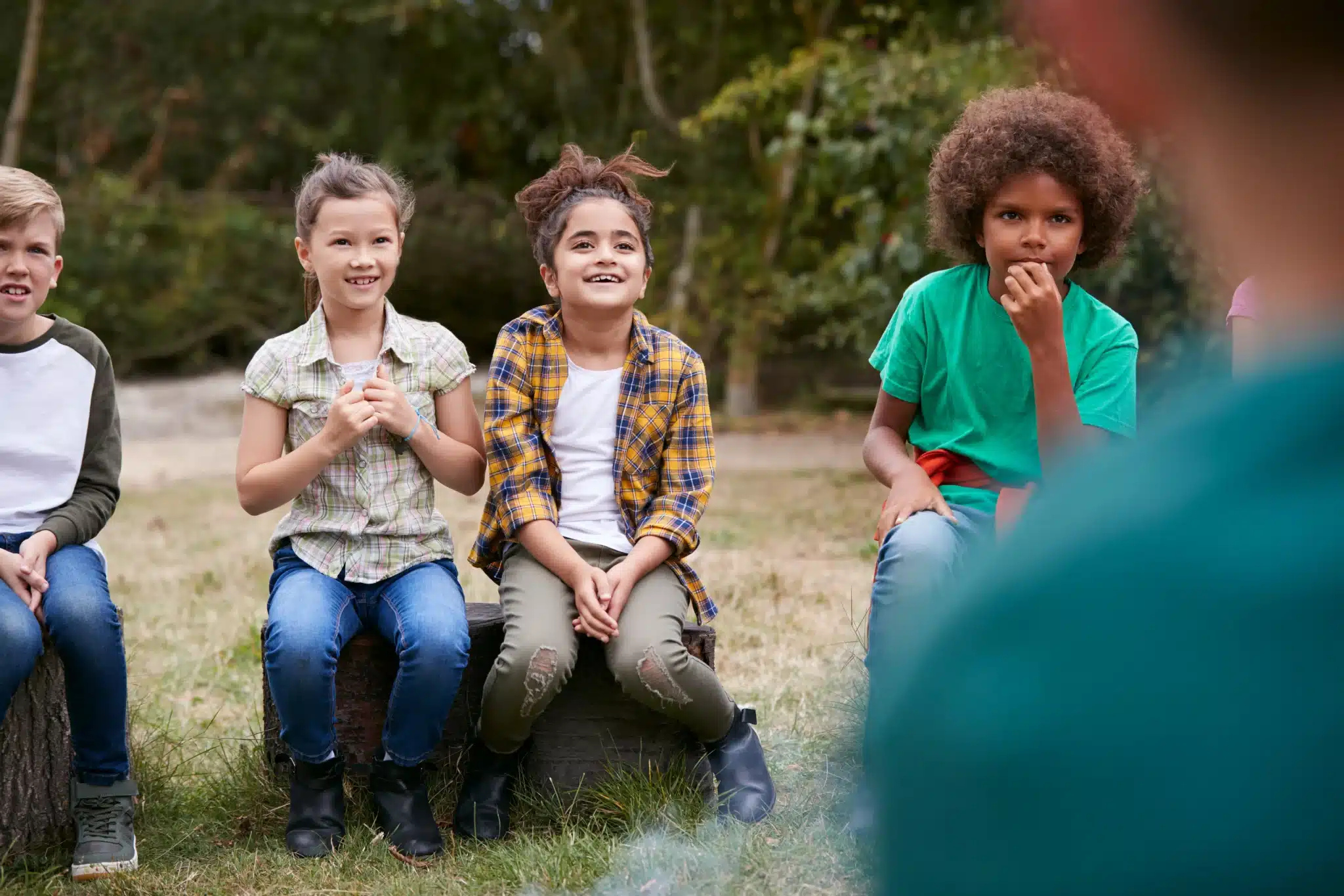 Children sitting outdoors and facing a person in the foreground