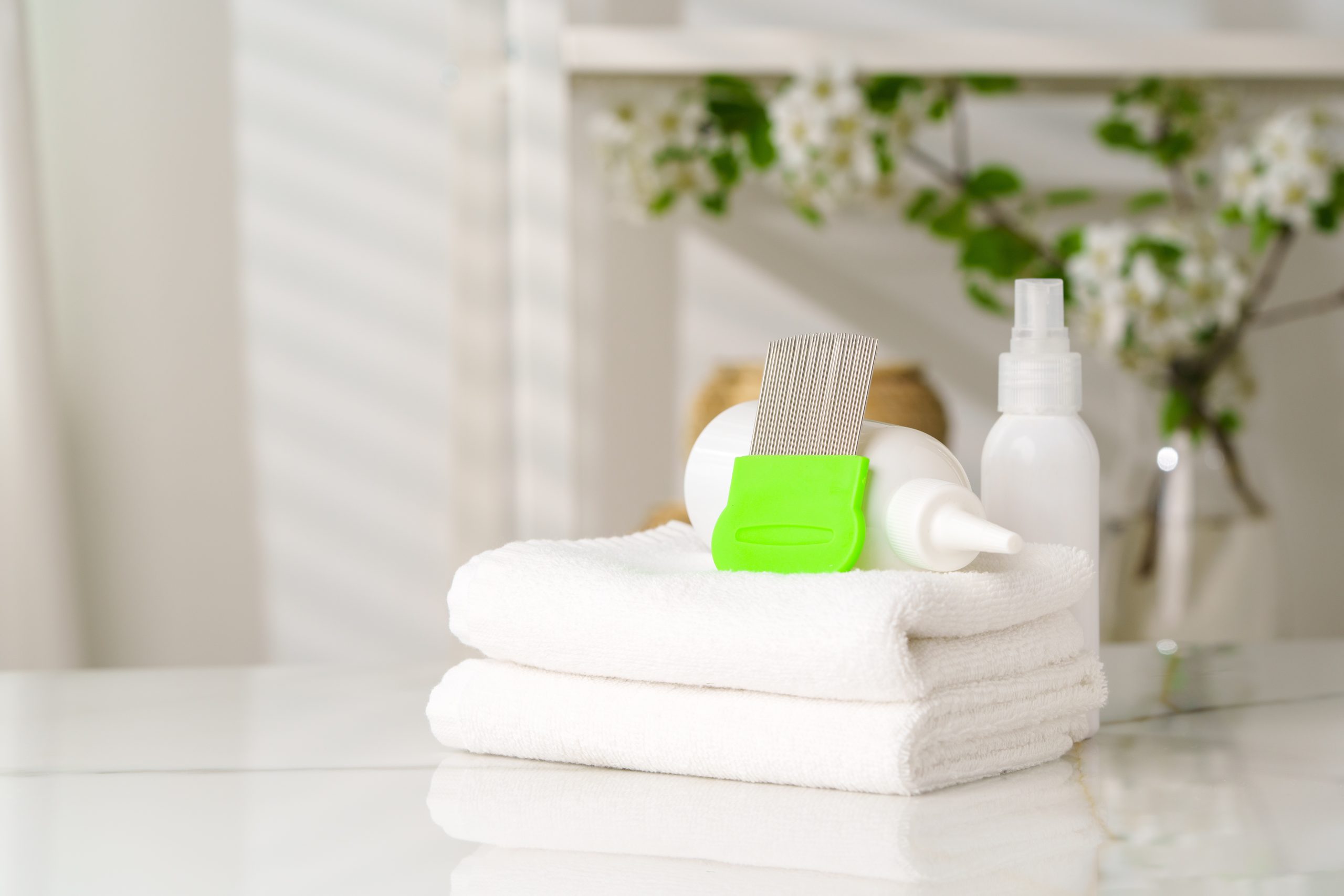 A green handled fine tooth comb and white containers on folded white towels.