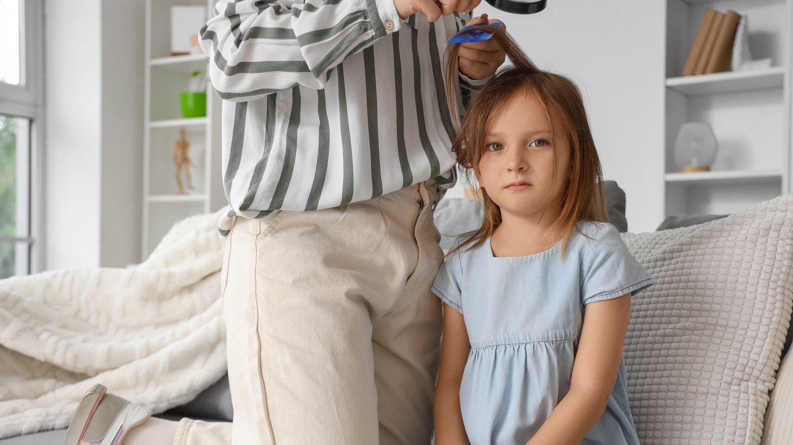 A mother examines her daughter's hair part line with a magnifying glass and a fine-toothed comb in soft home light, the at-home daylight lice check Travis County families do before reaching for any UV flashlight.