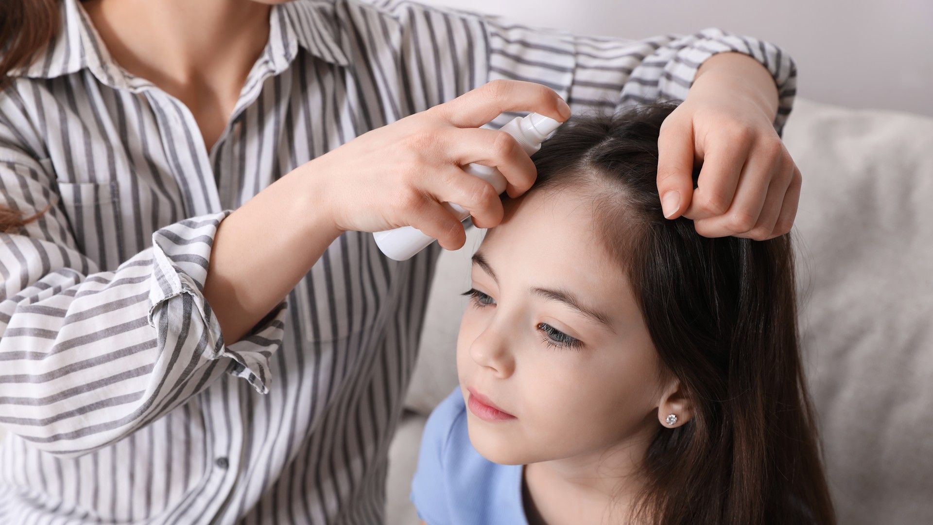 Person holding a spray bottle near another person's parted dark hair.