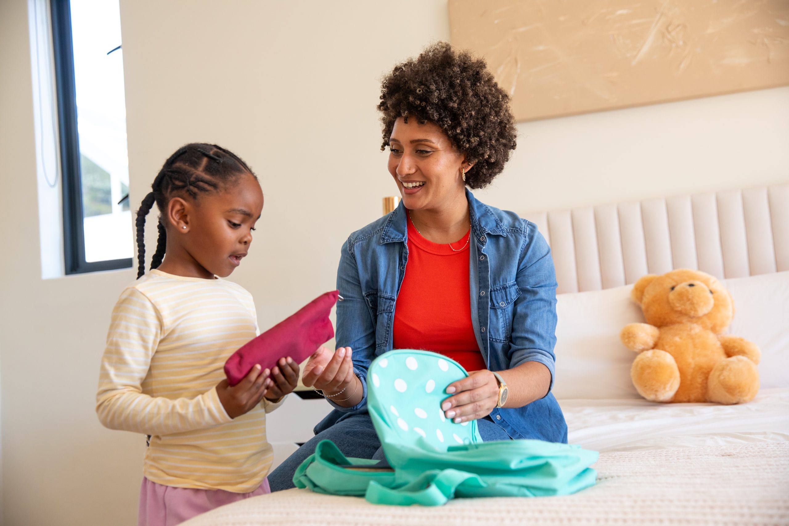 Mother and school-age daughter packing a backpack at home the morning before the school year starts.