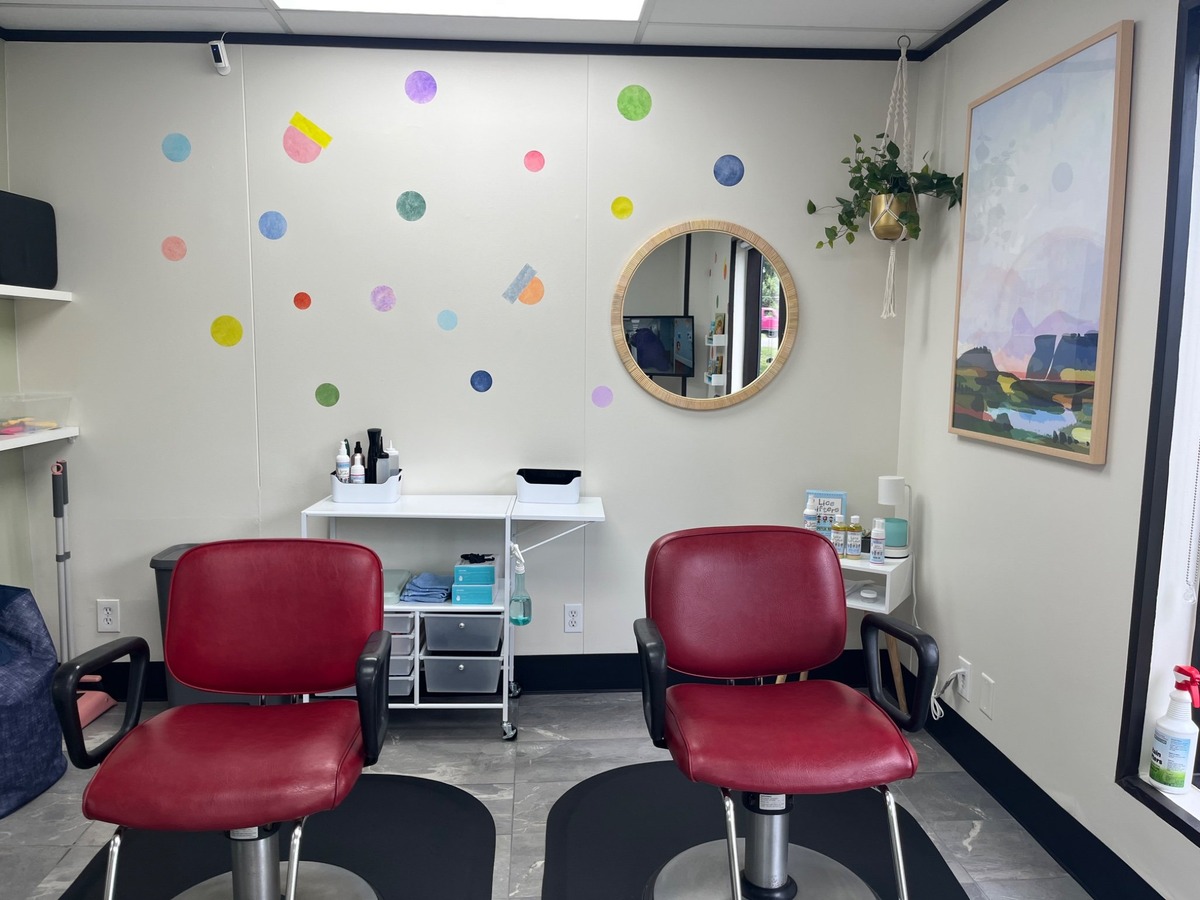 Two red chairs beside a supply cart beneath a round wall mirror