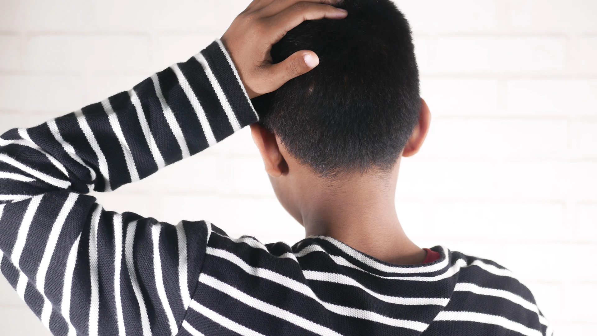 Person in a striped shirt touching the back of their head, viewed from behind.