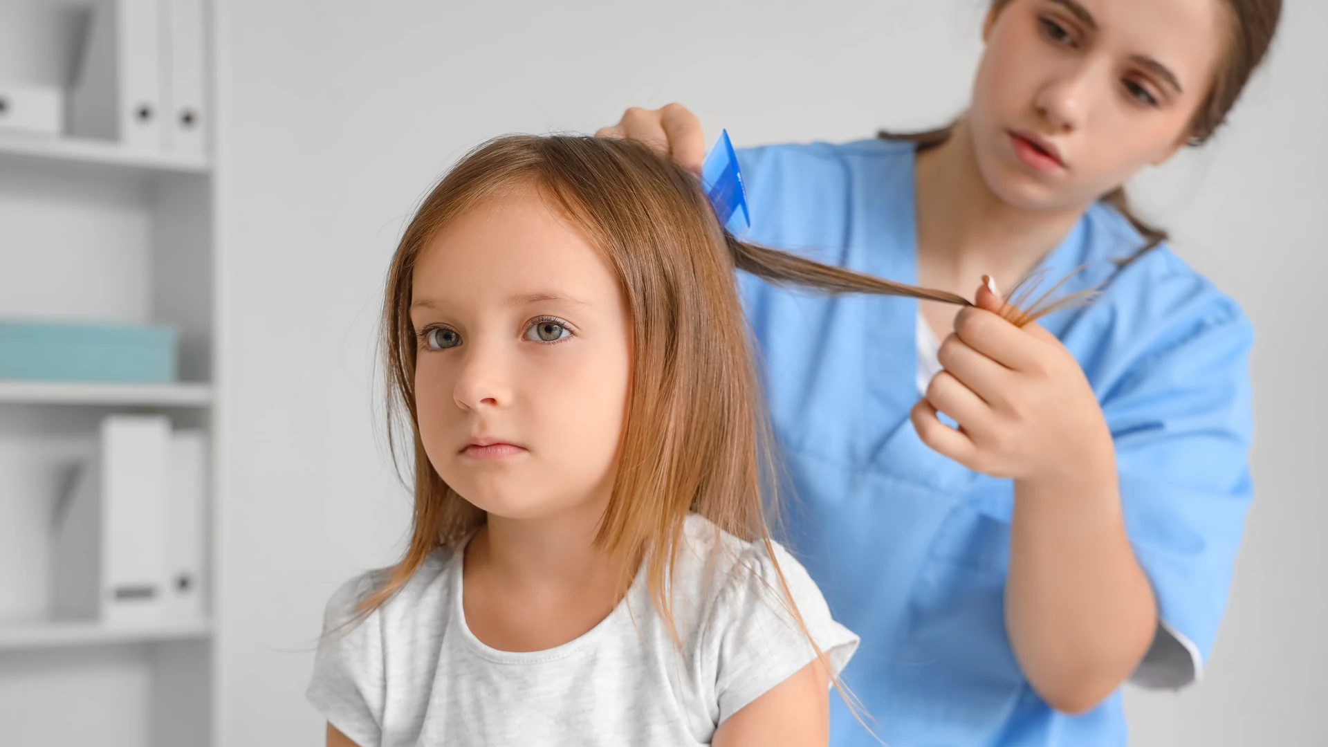 Person in blue clothing combing a section of another person's hair.