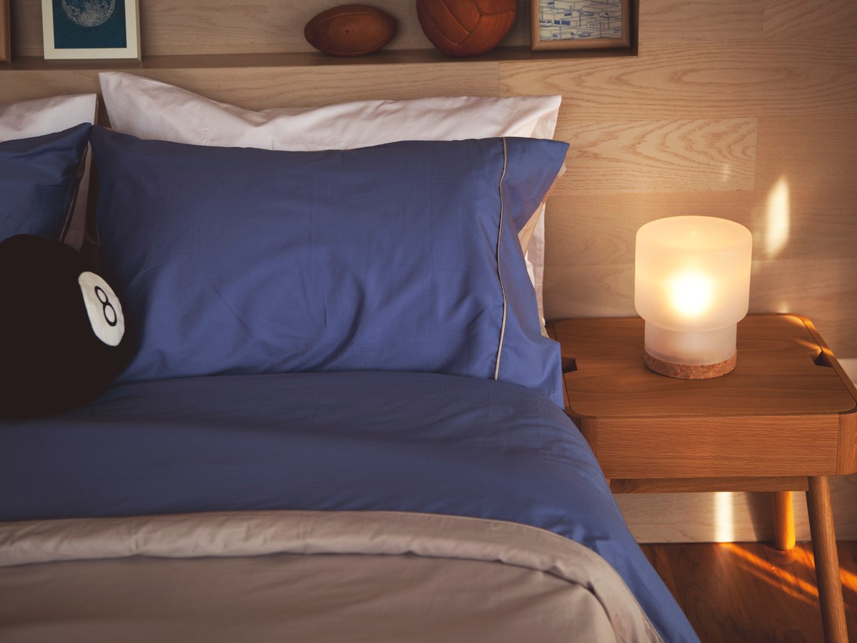 Bedside lamp glowing beside a made bed at night
